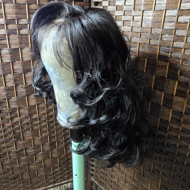 Long black loose-curl wig unit on a stand